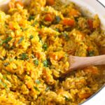 orange rice with pumpkin cubes and parsley in a white dutch oven