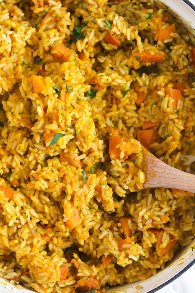 close up of pumpkin rice stirred with a wooden spoon