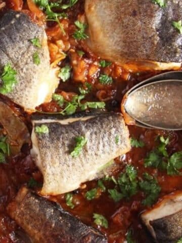 stewed trout with tomatoes in a skillet served with polenta in a bowl.