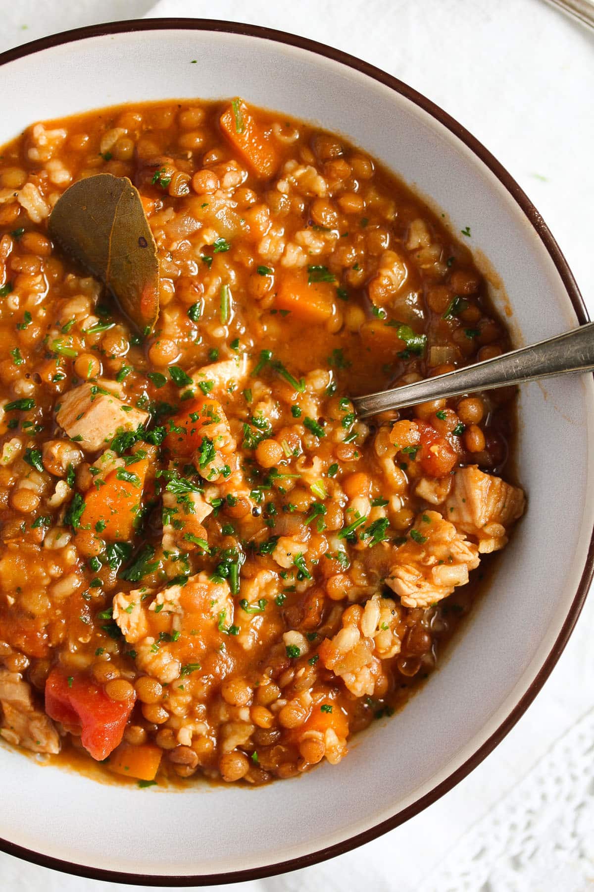 close up of hearty turkey lentil soup in a small white bowl with a spoon in it. 