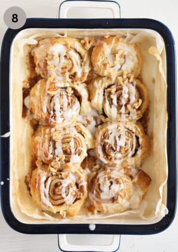 eight cinnamon and walnut rolls baked in a small baking dish and sprinkled with sugar icing.