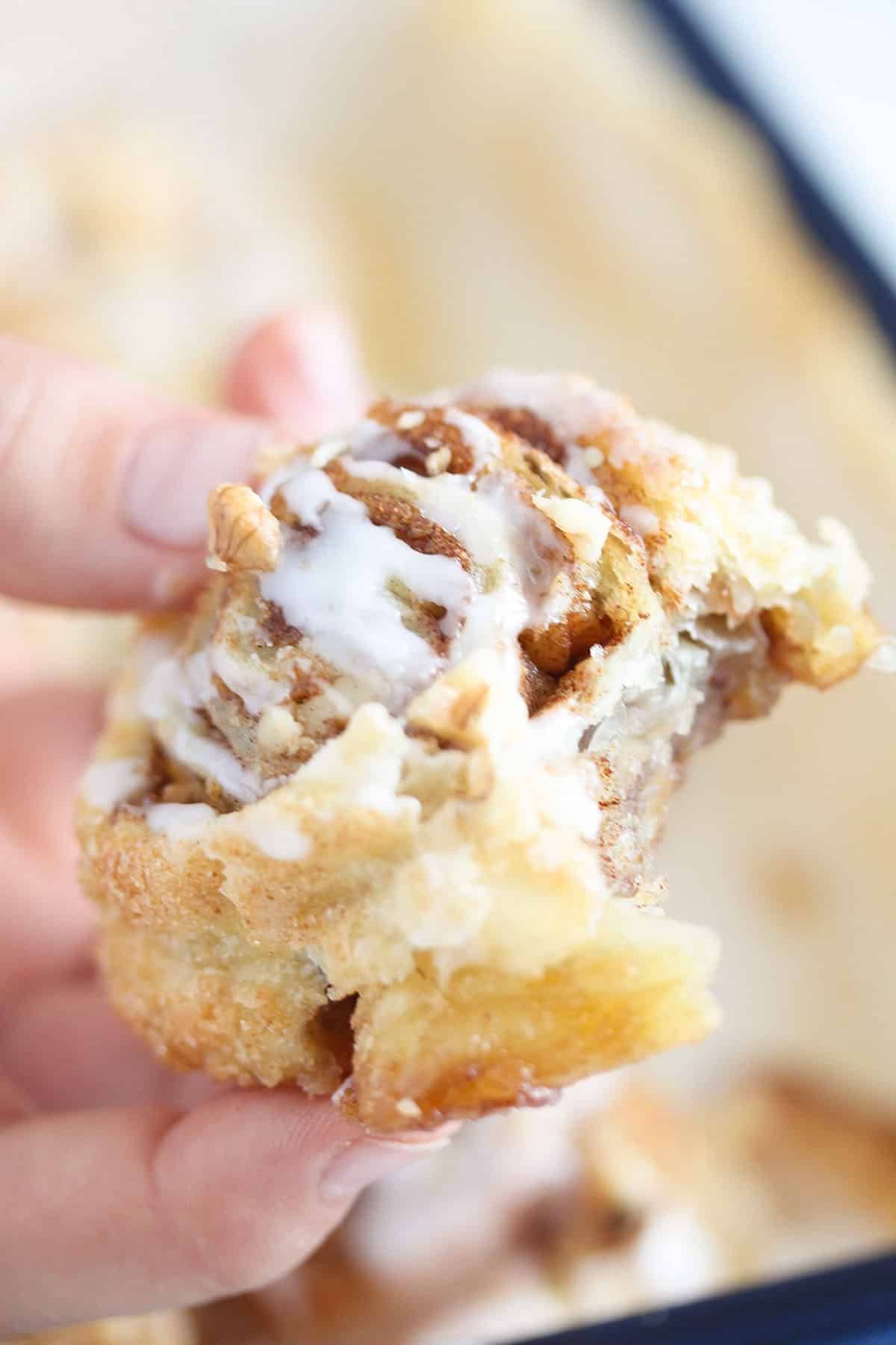 one hand holding one walnut swirls sprinkled with icing.