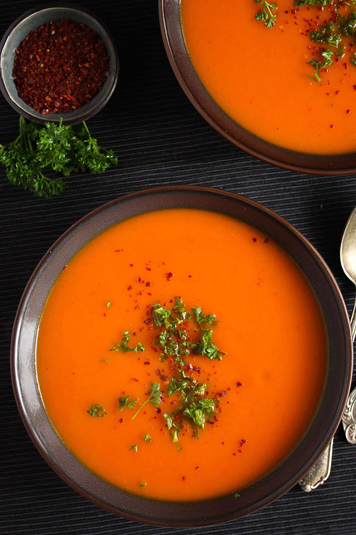 bowl of soup with butternut squash, red peppers, and carrots garnished with parsley.