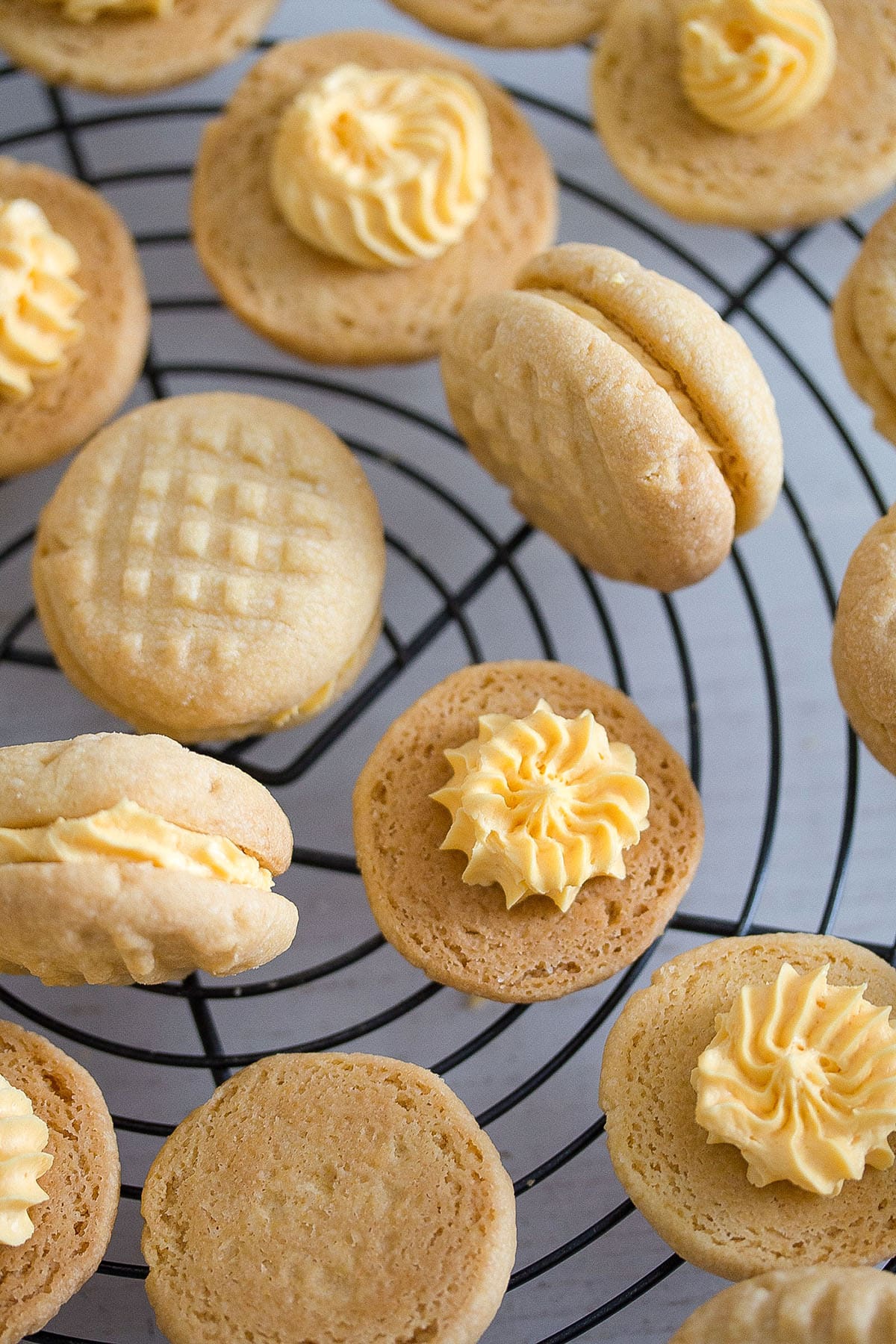 many custard cream biscuits on a wire rack, some showing the custard filling inside.