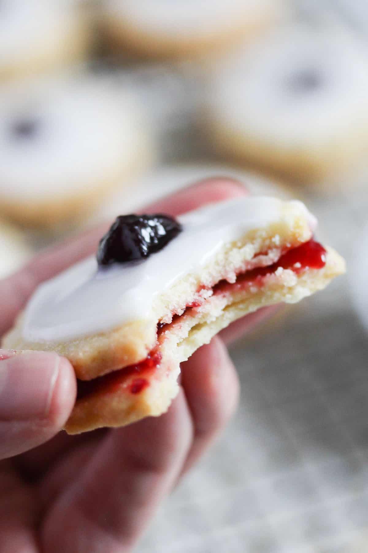 a hand holding a german empire biscuit with a glace cherry on top.