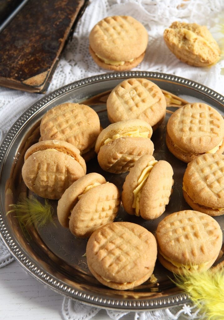 many custard cream biscuits on a silver plate with a vintange book beside