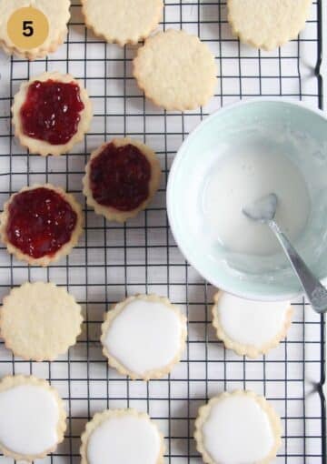cookies with jam and some covered with another iced cookie; a bowl of sugar icing beside.
