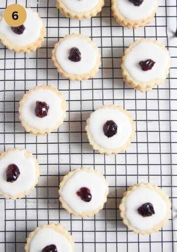 iced empire cookies decorated with candied cherries on a rack.