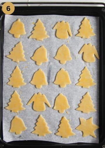 cookies cut out like trees and bells, smeared with egg on a baking tray before baking.