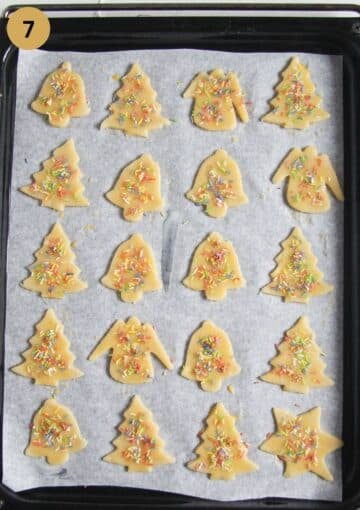 unbaked butter cookies topped with sprinkles on a baking sheet.