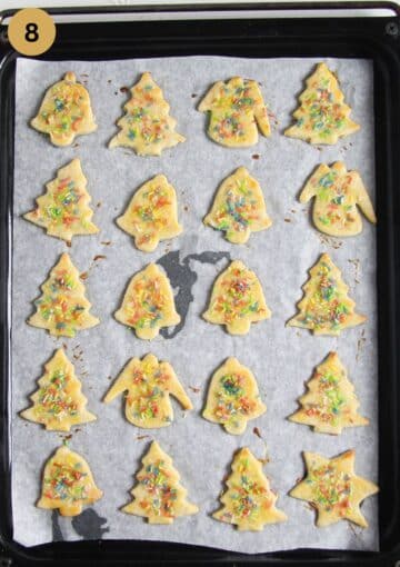 baked butter cookies shaped like bells and christmas tree on a baking sheet.