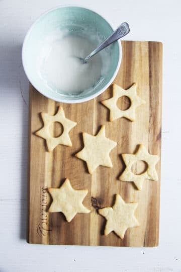 baked spitzbuben cookies and a bowl of sugar icing on a cutting board.