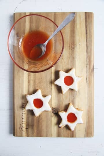 filled star-shaped jam cookies and a bowl of jam with a spoon in it.
