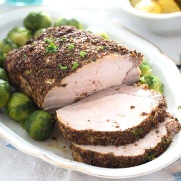 spicy pork roast sliced on a platter with brussels sprouts.