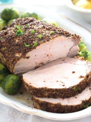 spicy pork roast sliced on a platter with brussels sprouts