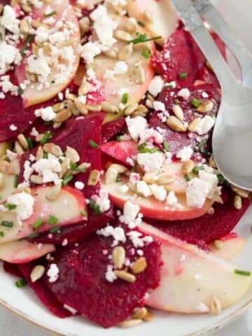 raw beetroot feta and apple salad on a platter with serving cutlery.