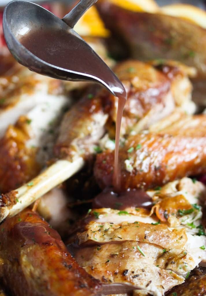 pouring red wine gravy on carved turkey