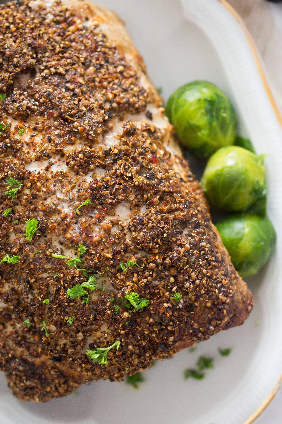 spicy crusted pork loin roast on a platter with three brussels sprouts.