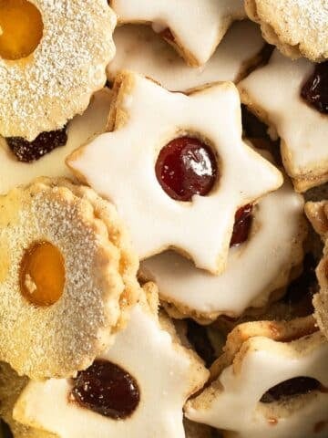 german spitzbuben cookies shaped like stards and round, filled with two types of jam and iced with sugar.