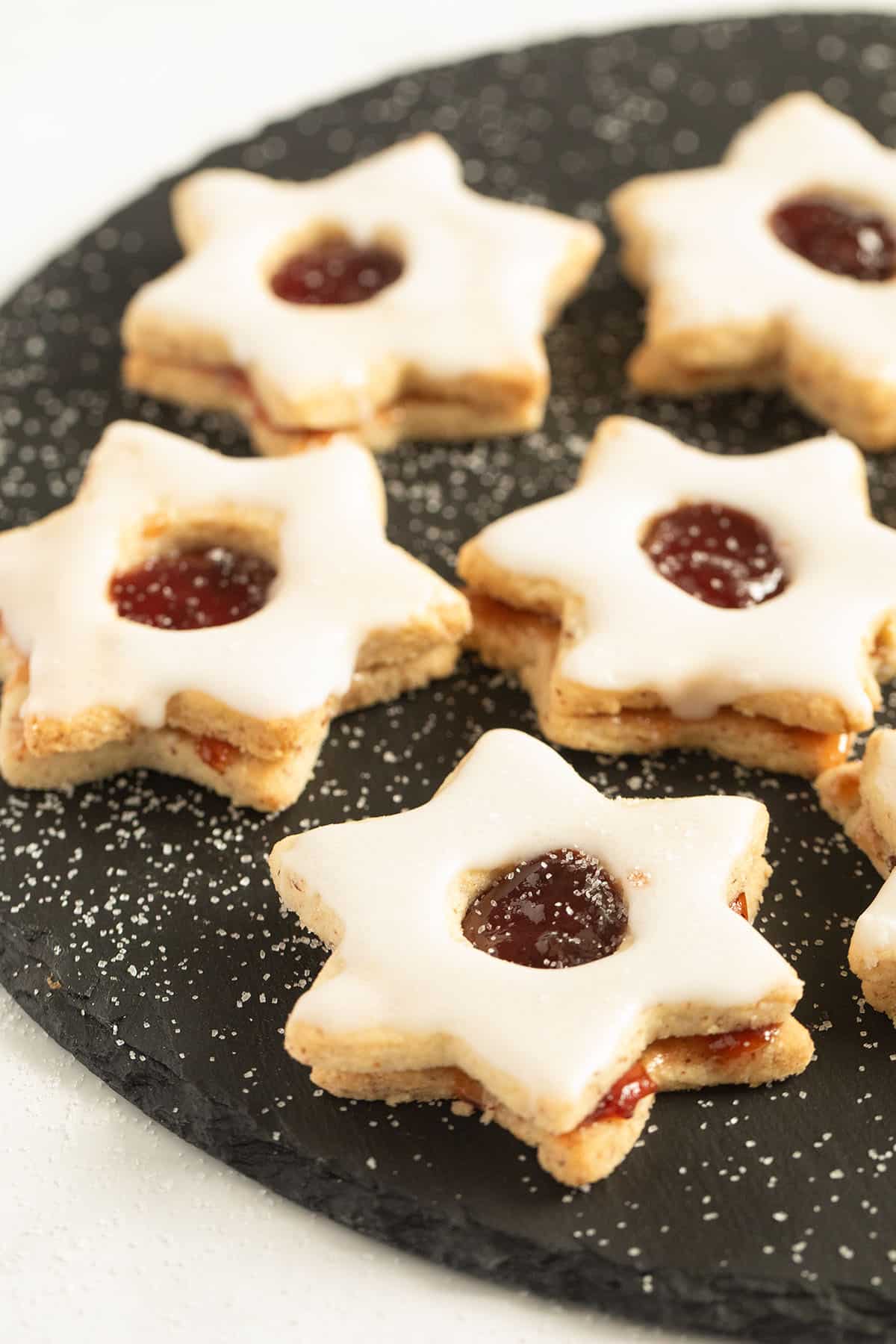 several star-shaped spitzbuben cookies filled withjam and iced with sugar on a round board.