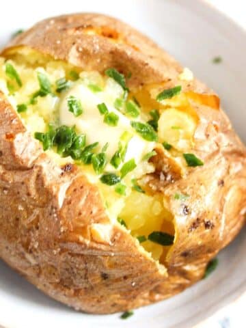 close up baked potato topped with melted butter and chives