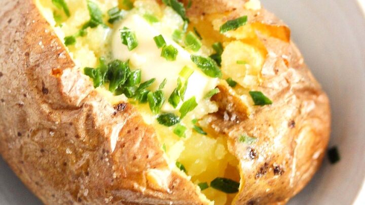 close up baked potato topped with melted butter and chives