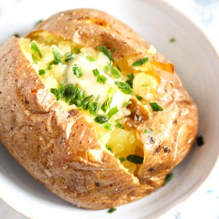 close up baked potato topped with melted butter and chives