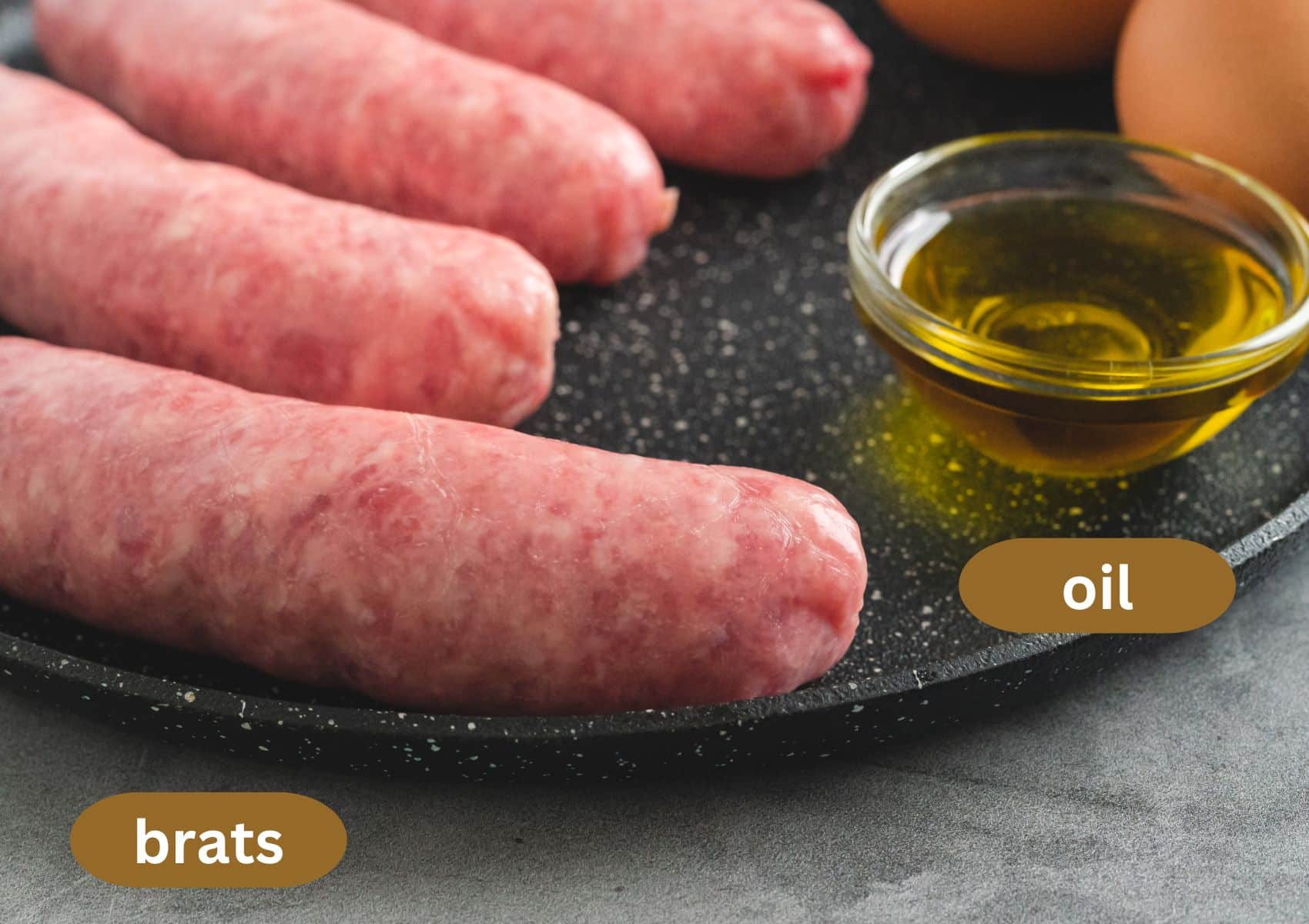 four raw bratwurst sausages and a small bowl of oil on a plate.