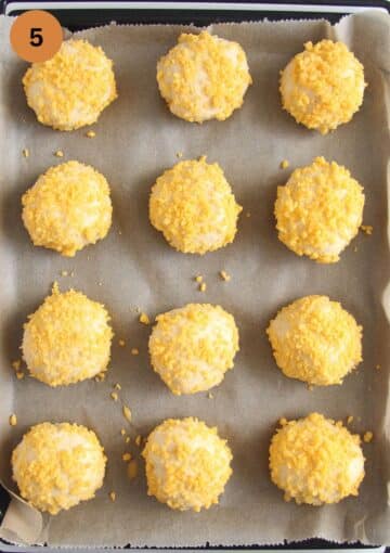 unbaked buns rolled in cheddar cheese on a baking sheet.