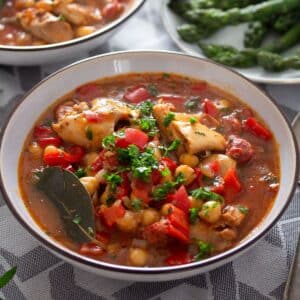 a bowl full of chickpea and chicken stew sprinkled with parsley.