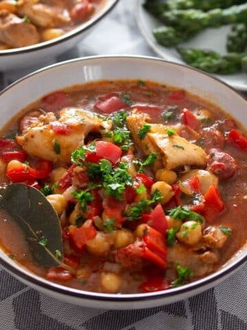 a bowl full of chickpea and chicken stew sprinkled with parsley.