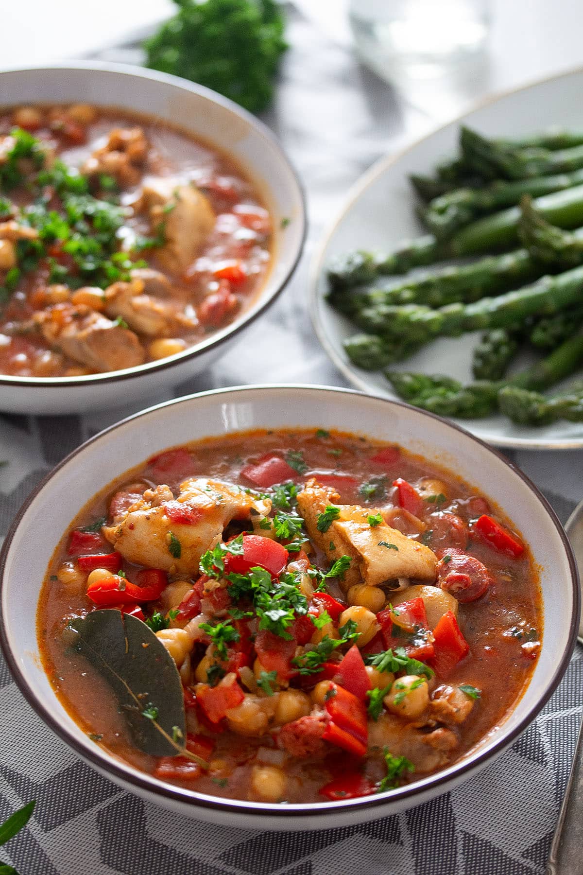 bowls of chickpeas chickens stew and a plate with asparagus behind them.