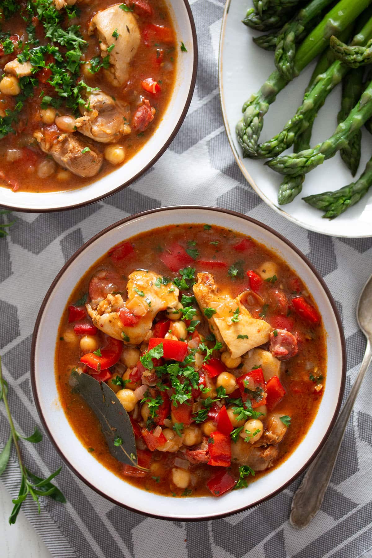 two bowls of chicken and chickpea stew and a platter of cooked asparagus.