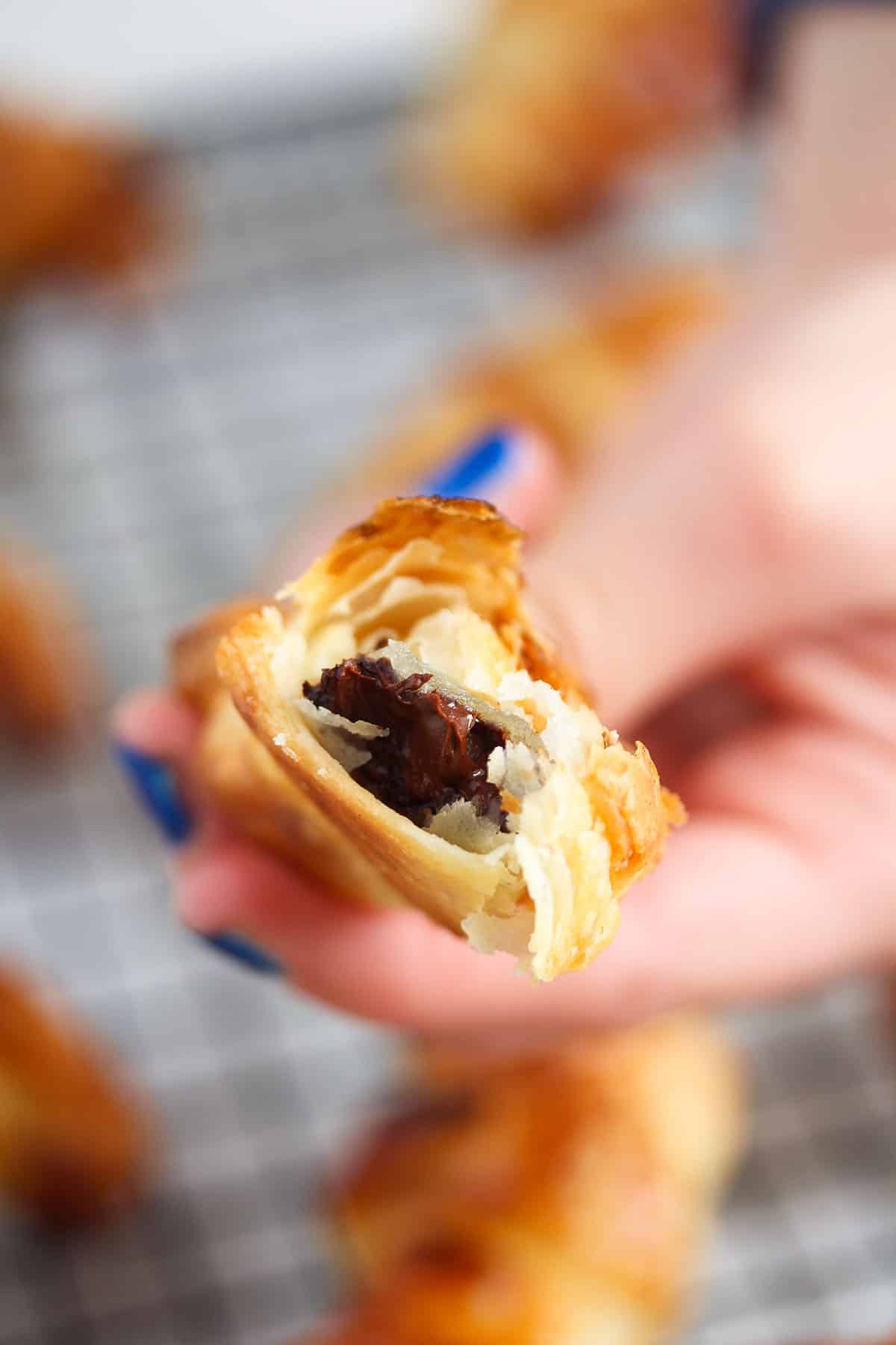 one chocolate puff pastry held by a hand with blue painted fingernails.