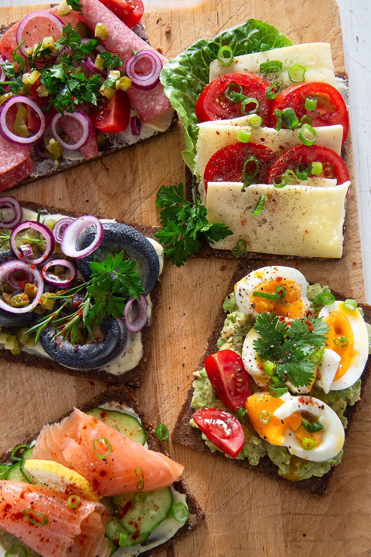 five danish sandwiches with different toppings on a cuttting board.