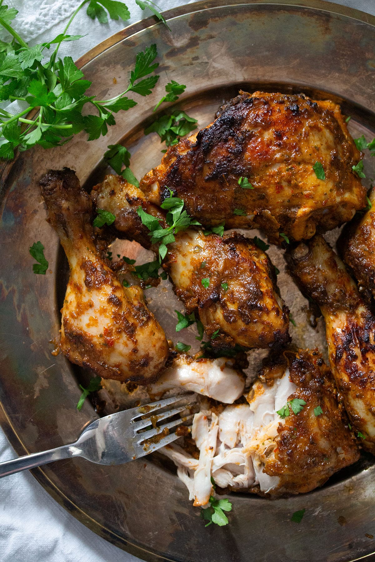 spicy peri peri chicken thighs on a platter with a fork and parsley.