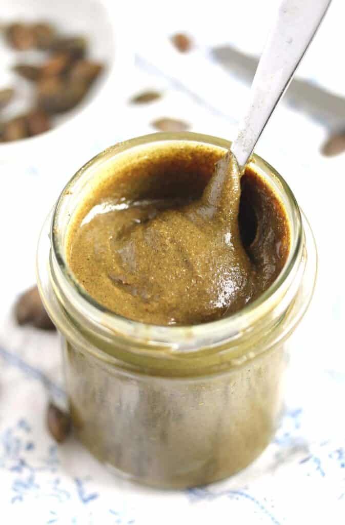 tall jar of creamy pumpkin seed butter with a spoon sticking in it.