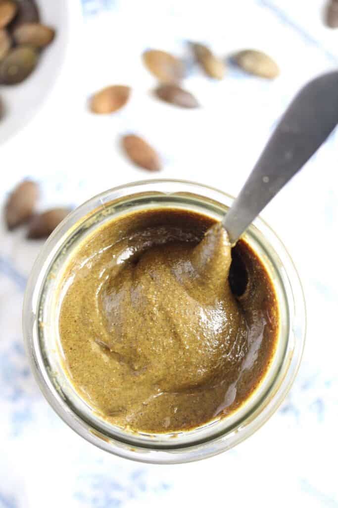 overhead view of an open jar with creamy pumpkin seed butter with a spoon in it.