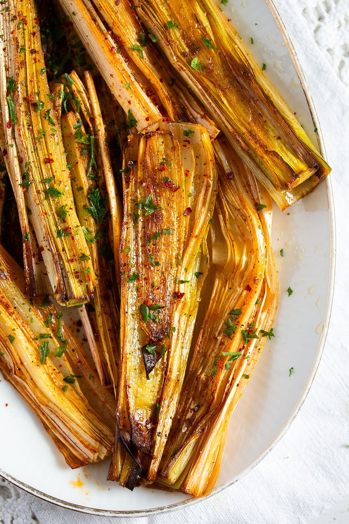 platter with baked leeks sprinkled with parsley and chili flakes.