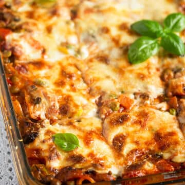 golden and sliced lasagna in a baking dish topped with basil.