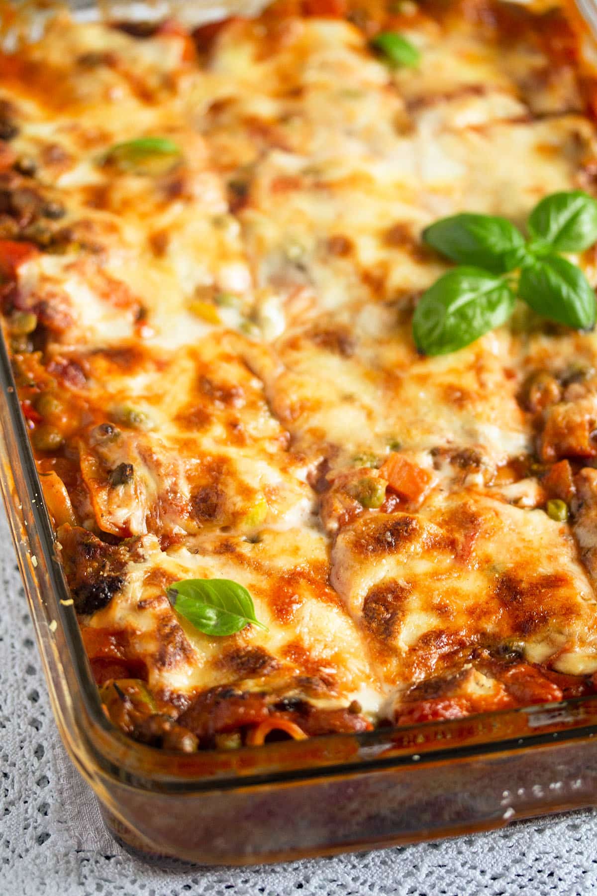 golden and sliced lasagna in a baking dish topped with basil.