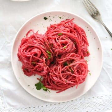 beetroot pasta on a small white plate sprinkled with parsley.