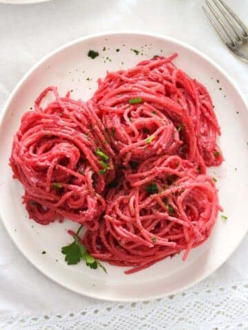 beetroot pasta on a small white plate sprinkled with parsley.