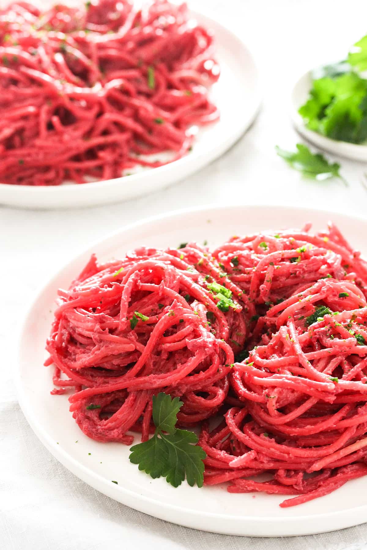 two plates holding spaghetti coated with pink beetroot sauce.