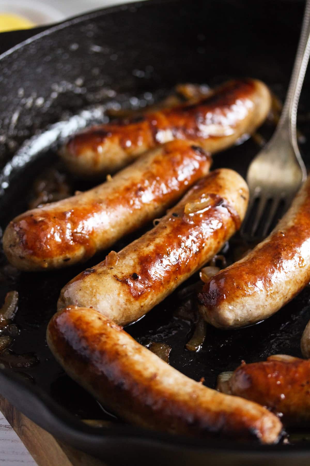 golden brown beer brats and a fork in a skillet on the stove.