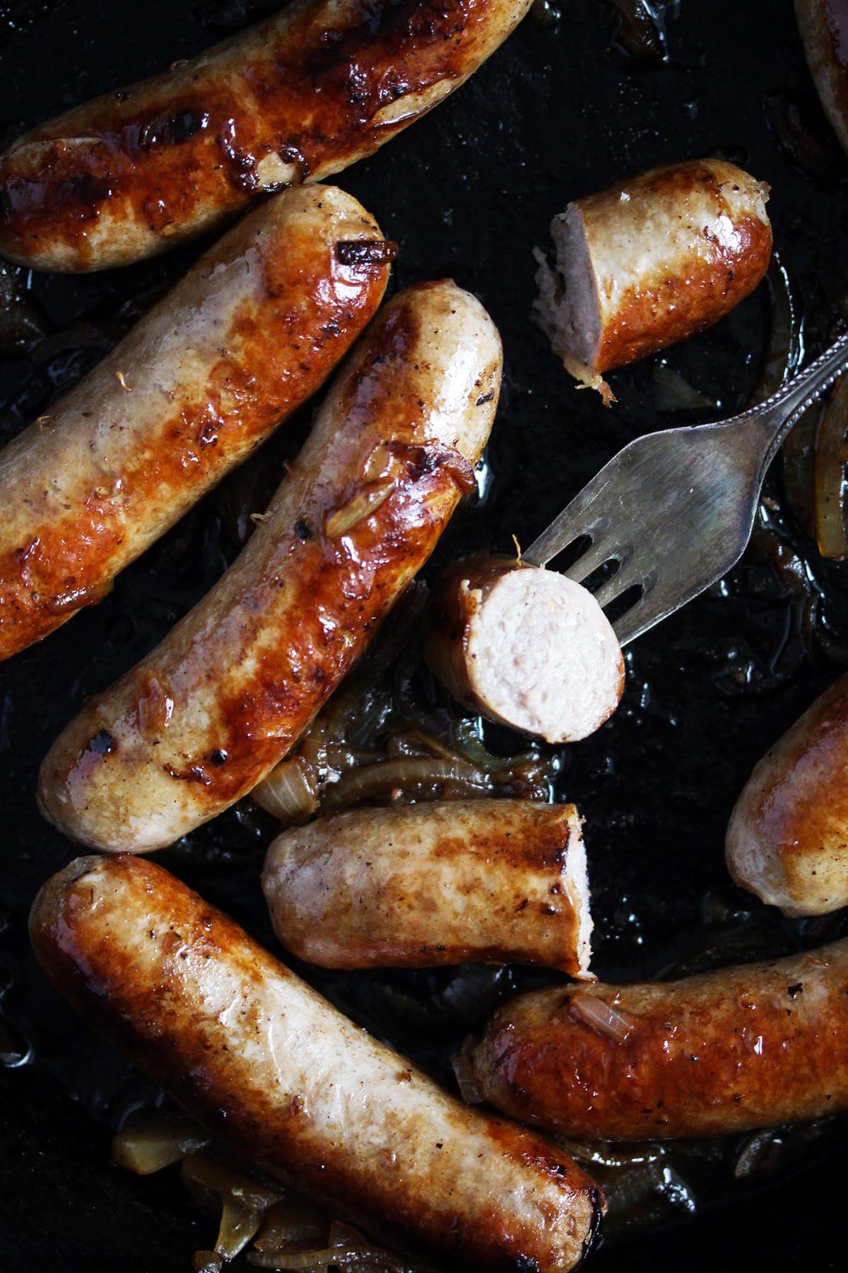 several brown cooked brats, one slice held by a fork.