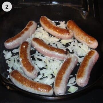half-cooked bratwursts with uncooked onions in a cast iron skillet.