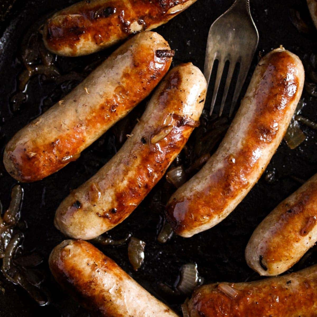 Close up of browned brats in a cast iron pan cooked with beer and onions.
