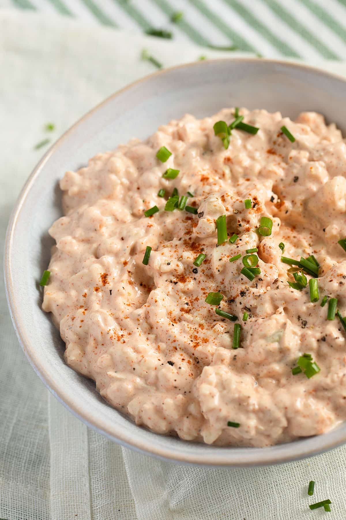 a bowl full of camembert spread or dip garnished with chopped green onions and sweet paprika.