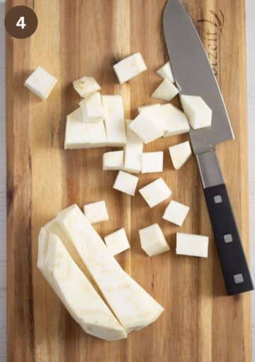 chopped celeriac pieces and a knife on a wooden board.